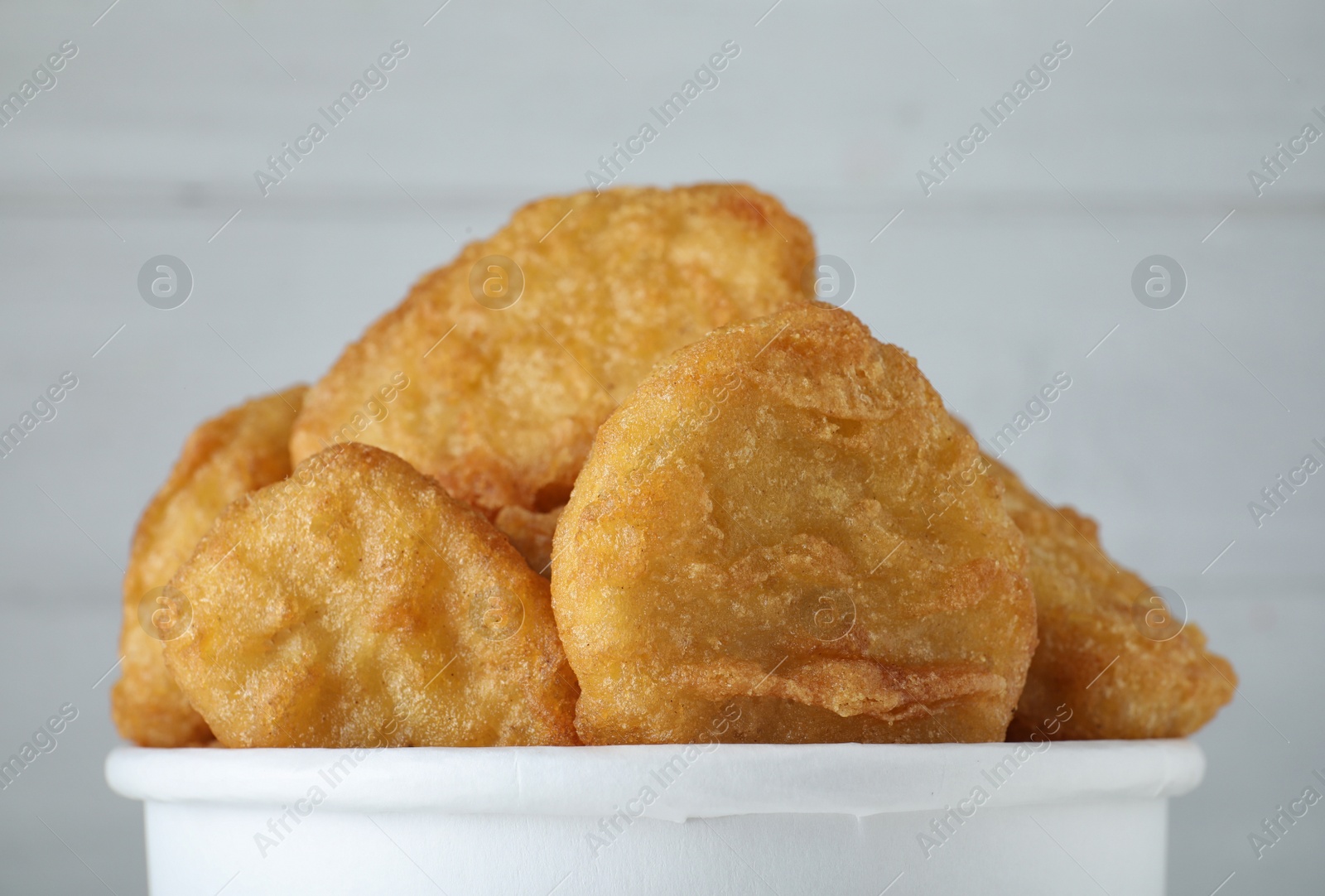 Photo of Bucket with tasty chicken nuggets on white wooden background, closeup