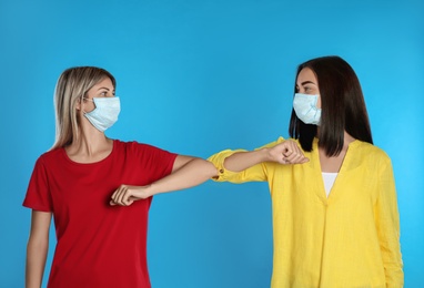 Women bumping elbows to say hello on light blue background. Keeping social distance during coronavirus pandemic