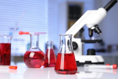 Laboratory analysis. Glass flasks with red liquid and microscope on white table indoors