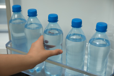 Woman taking bottle of fresh water from fridge door bin, closeup