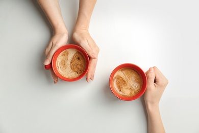 Photo of Young women with cups of delicious hot coffee on light background, top view