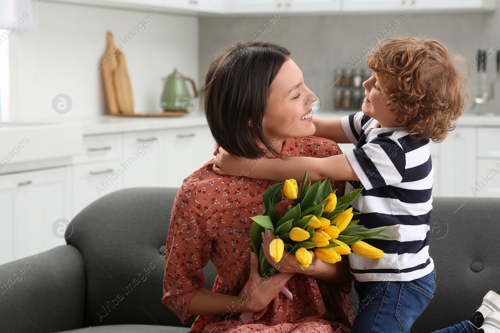 Photo of Little son congratulating his mom with Mother`s day at home. Woman holding bouquet of yellow tulips