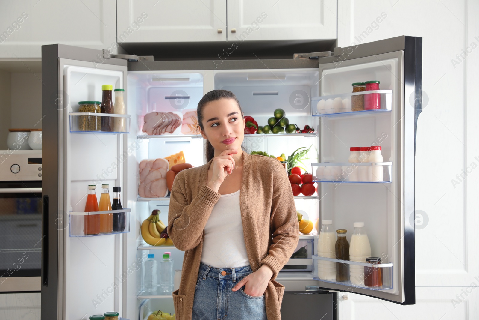 Photo of Thoughtful young woman near open refrigerator in kitchen