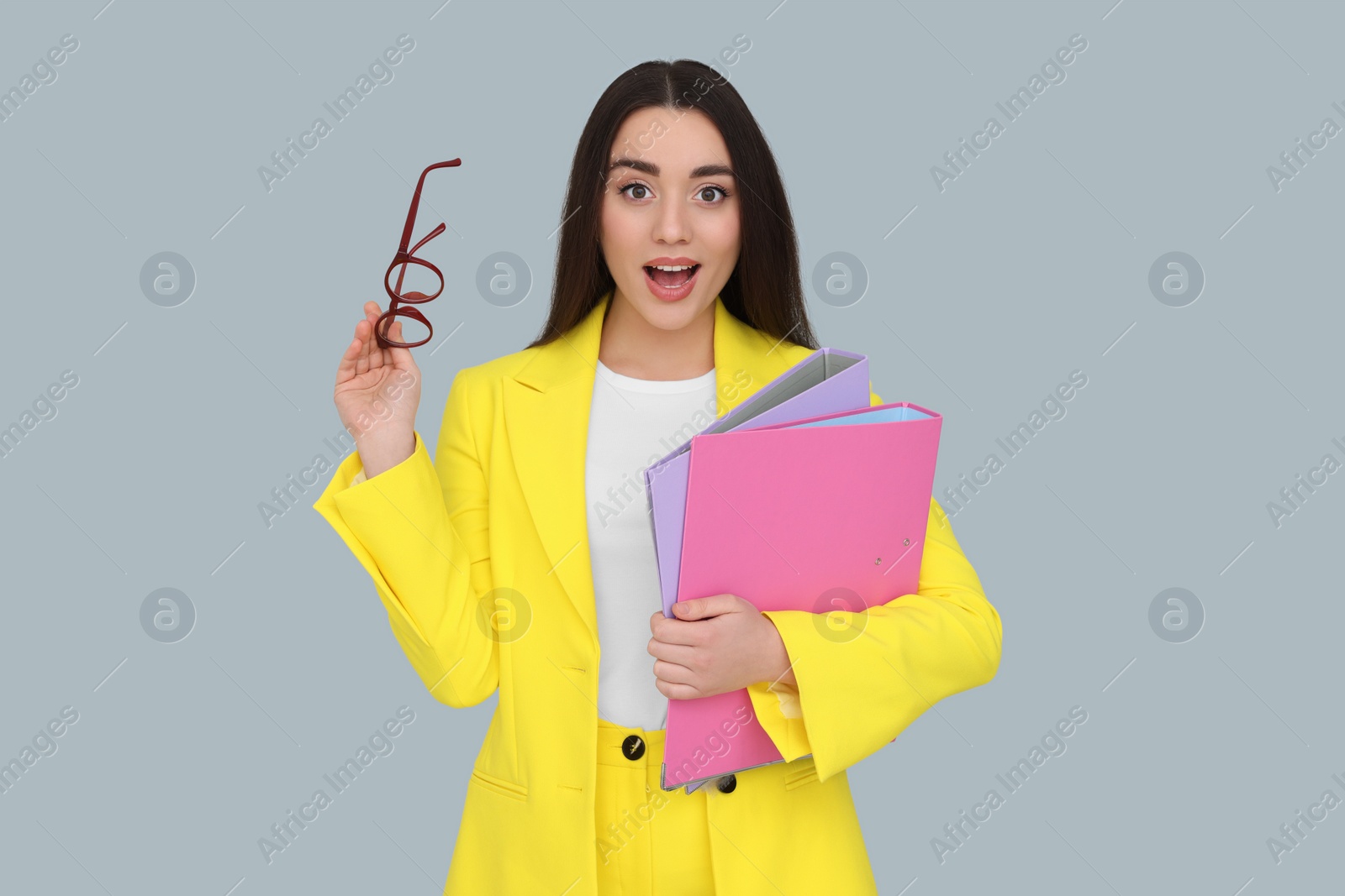 Photo of Young female intern with eyeglasses and folders on grey background