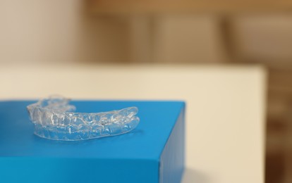 Transparent dental aligner on blurred background, closeup. Space for text