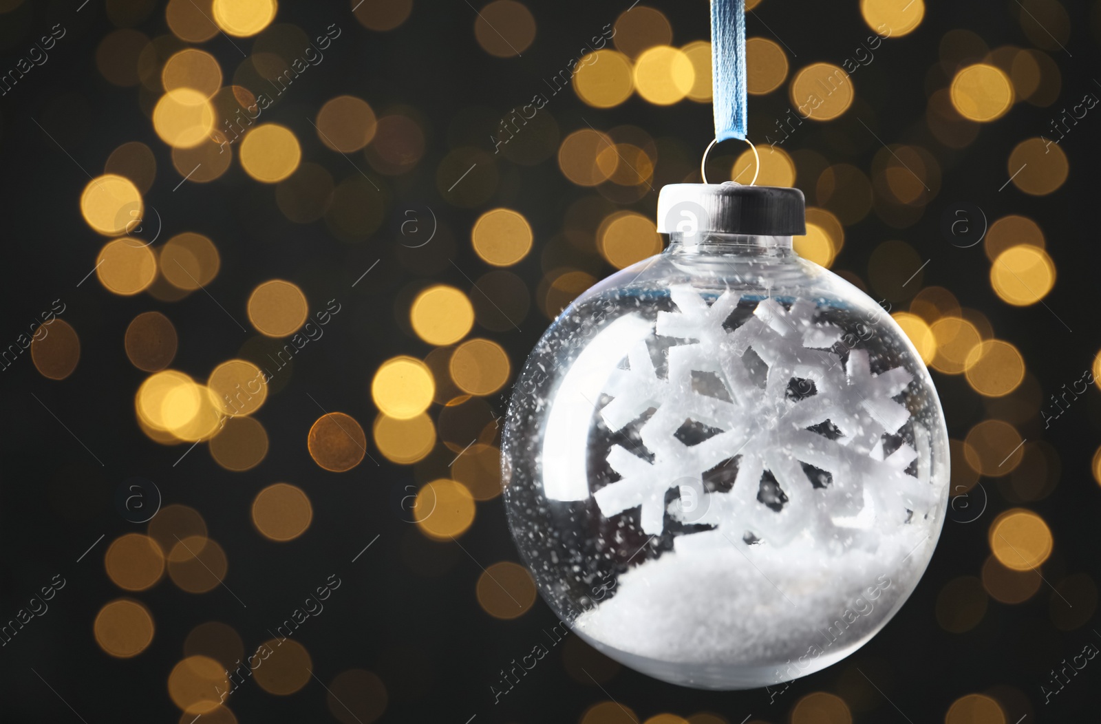 Photo of Decorative snow globe hanging against blurred festive lights, closeup. Space for text