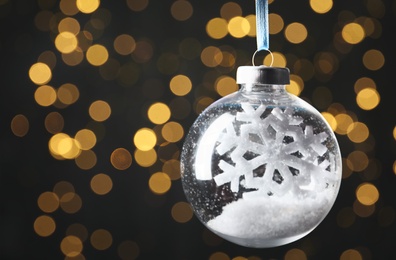 Photo of Decorative snow globe hanging against blurred festive lights, closeup. Space for text