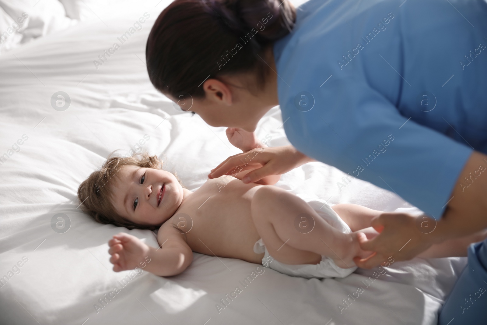 Photo of Orthopedist examining cute little baby on bed