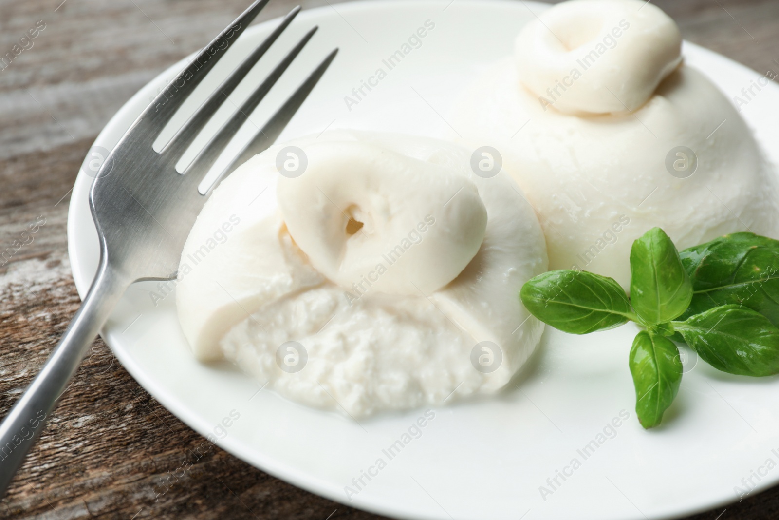 Photo of Delicious burrata cheese with basil on wooden table, closeup