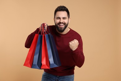 Photo of Happy man with many paper shopping bags on beige background