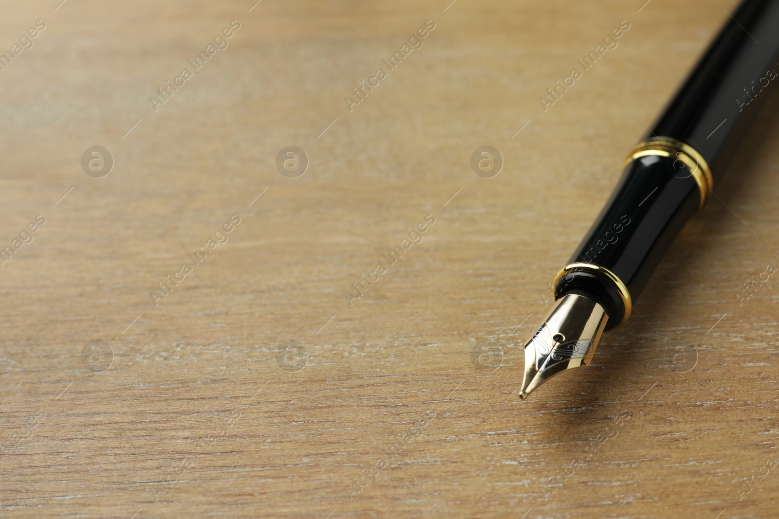 Photo of Stylish fountain pen on wooden table, closeup. Space for text