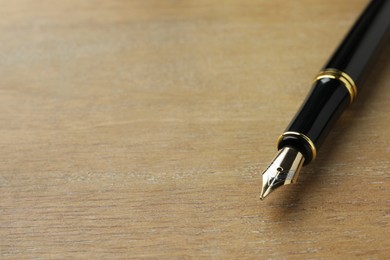 Photo of Stylish fountain pen on wooden table, closeup. Space for text