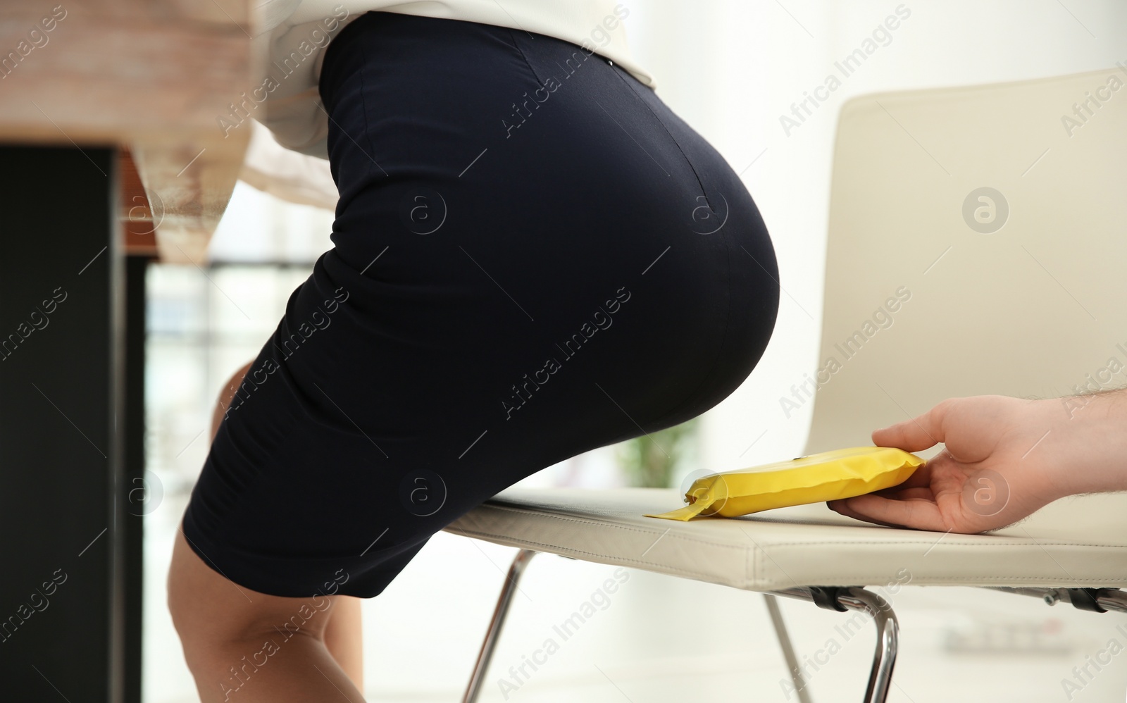 Photo of Young man putting whoopee cushion on chair while his colleague sitting down in office, closeup. Funny joke