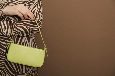 Photo of Woman with stylish baguette handbag on brown background, closeup. Space for text