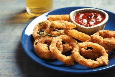 Photo of Plate with homemade crunchy fried onion rings and tomato sauce on wooden background, closeup