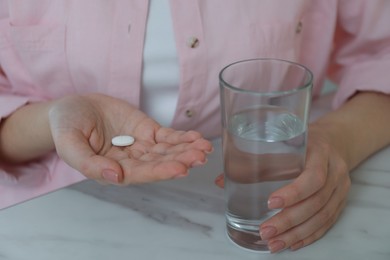 Young woman with abortion pill and glass of water at white marble table, closeup