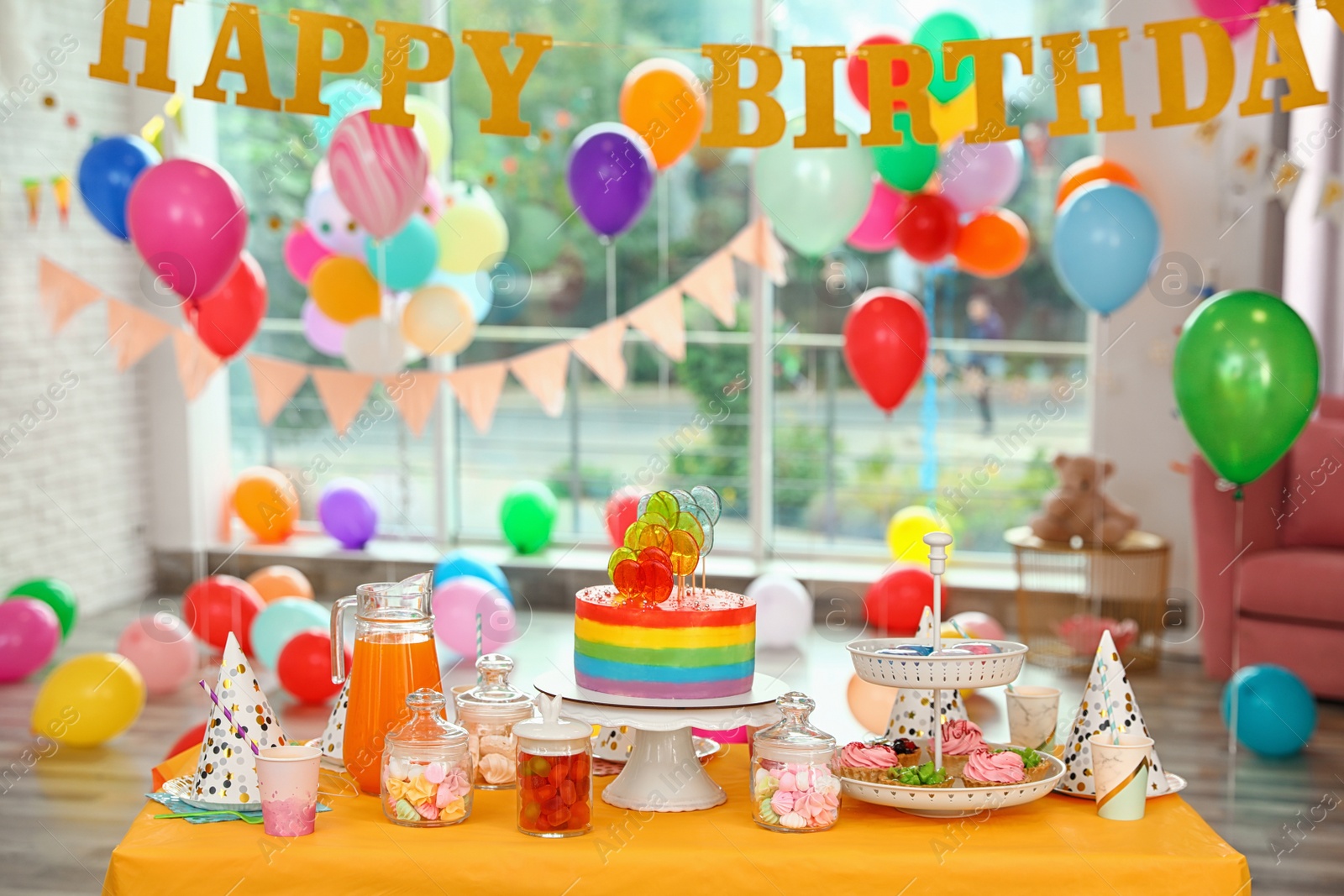 Photo of Bright birthday cake and other treats on table in decorated room