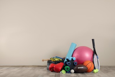 Set of different sports equipment on floor near beige wall, space for text