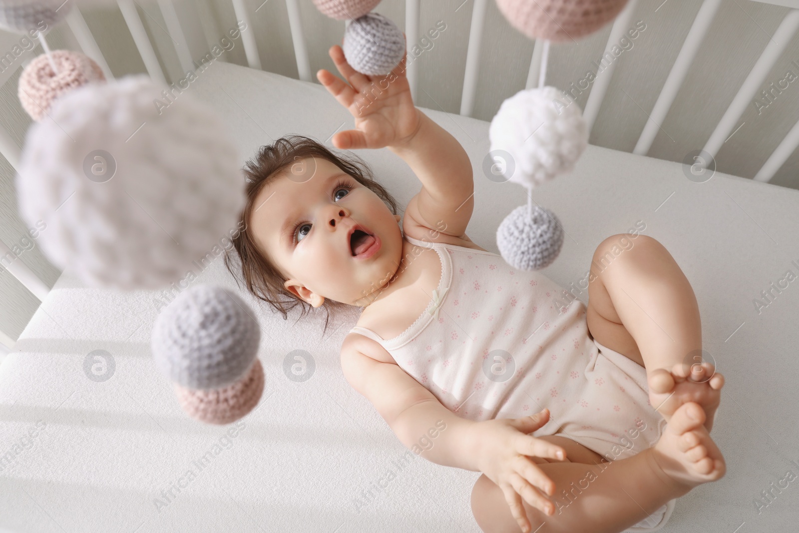 Photo of Cute little baby looking at hanging mobile in crib, top view