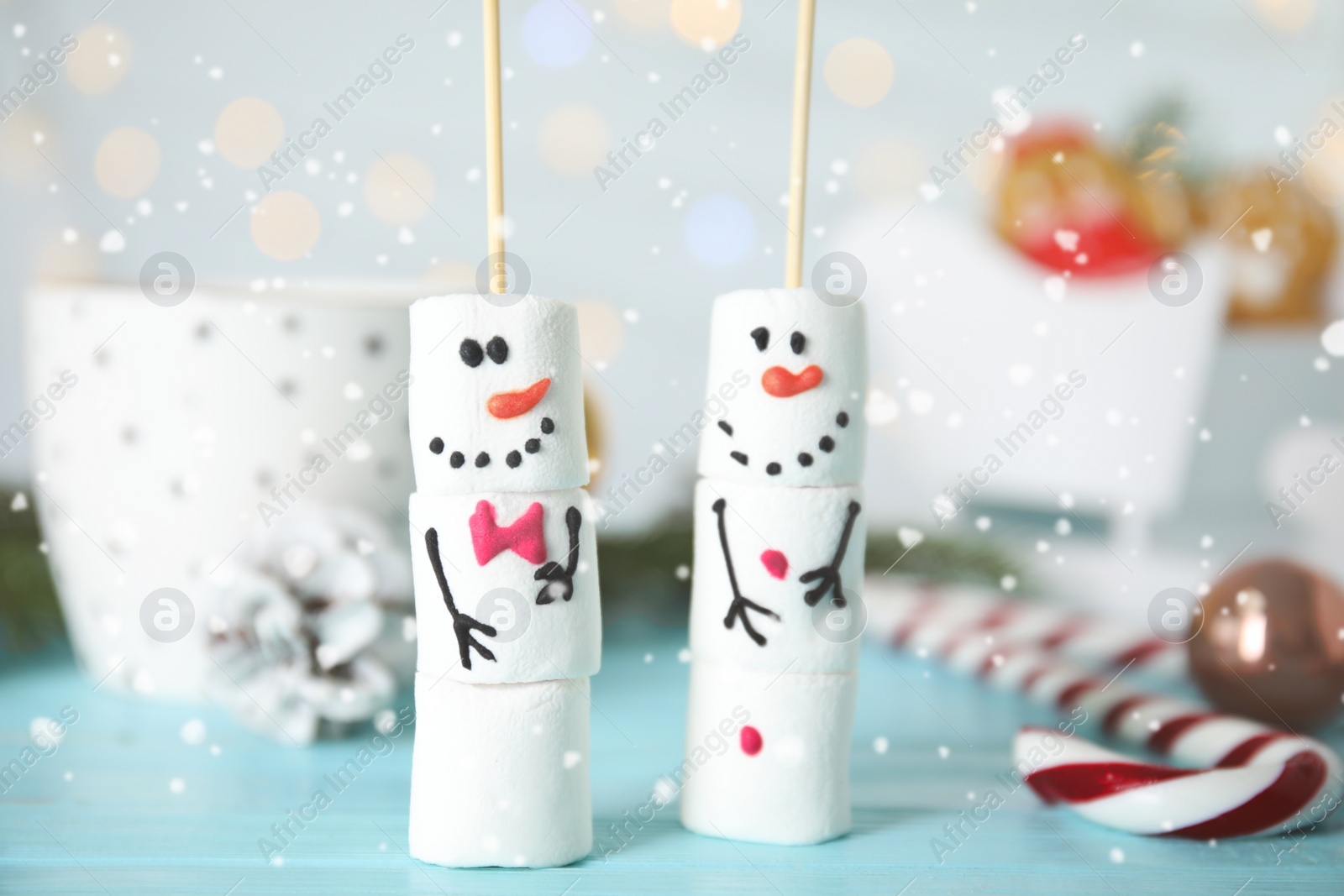 Photo of Funny snowmen made of marshmallows on light blue wooden table, closeup