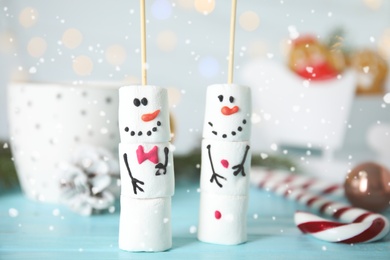 Photo of Funny snowmen made of marshmallows on light blue wooden table, closeup