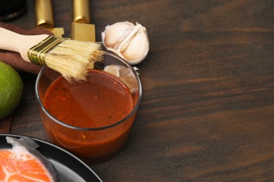 Photo of Tasty fish marinade, basting brush and products on wooden table, closeup. Space for text