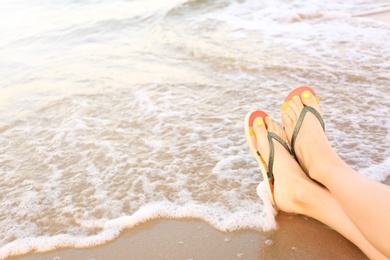 Photo of Closeup of woman with stylish flip flops on sand near sea, space for text. Beach accessories