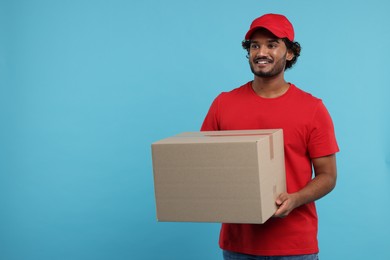 Happy young courier with parcel on light blue background, space for text