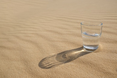 Glass of water on sand in desert. Space for text