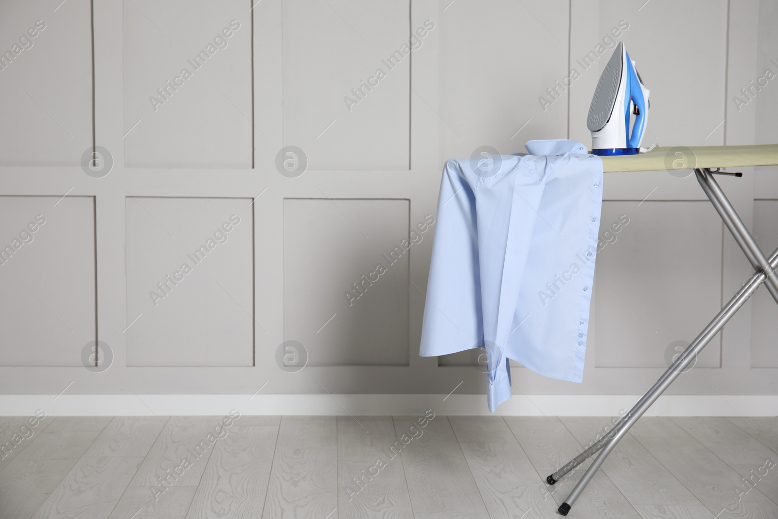 Photo of Modern iron and clean shirt on board indoors, space for text