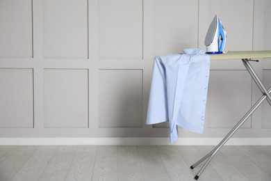 Photo of Modern iron and clean shirt on board indoors, space for text