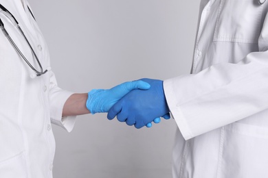 Photo of Doctors shaking hands on light grey background, closeup