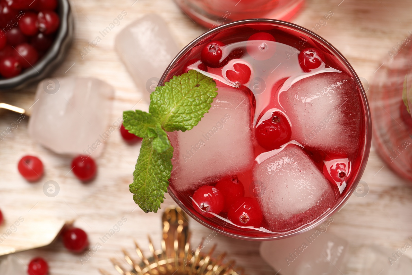 Photo of Tasty cranberry cocktail with ice cubes and mint in glass on light table, flat lay