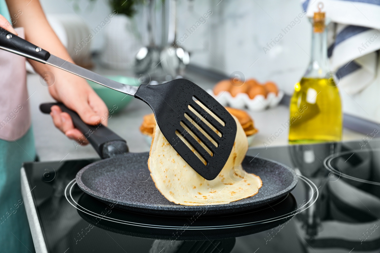 Photo of Woman cooking delicious thin pancakes on induction stove, closeup