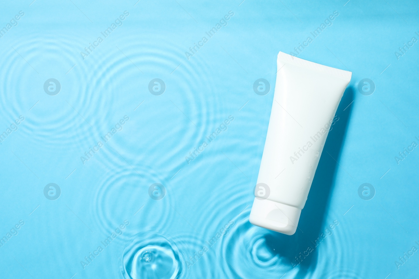 Photo of Tube with moisturizing cream in water on light blue background, top view. Space for text