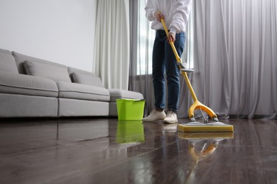 Photo of Woman cleaning parquet floor with mop indoors, closeup