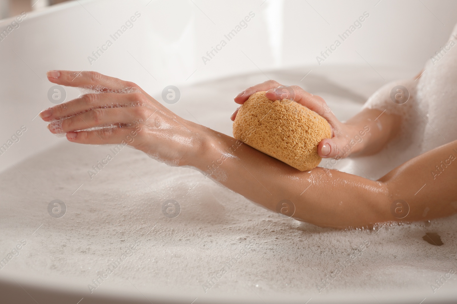 Photo of Woman rubbing her forearm with sponge while taking bath, closeup