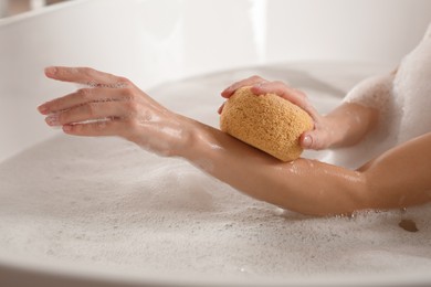 Photo of Woman rubbing her forearm with sponge while taking bath, closeup