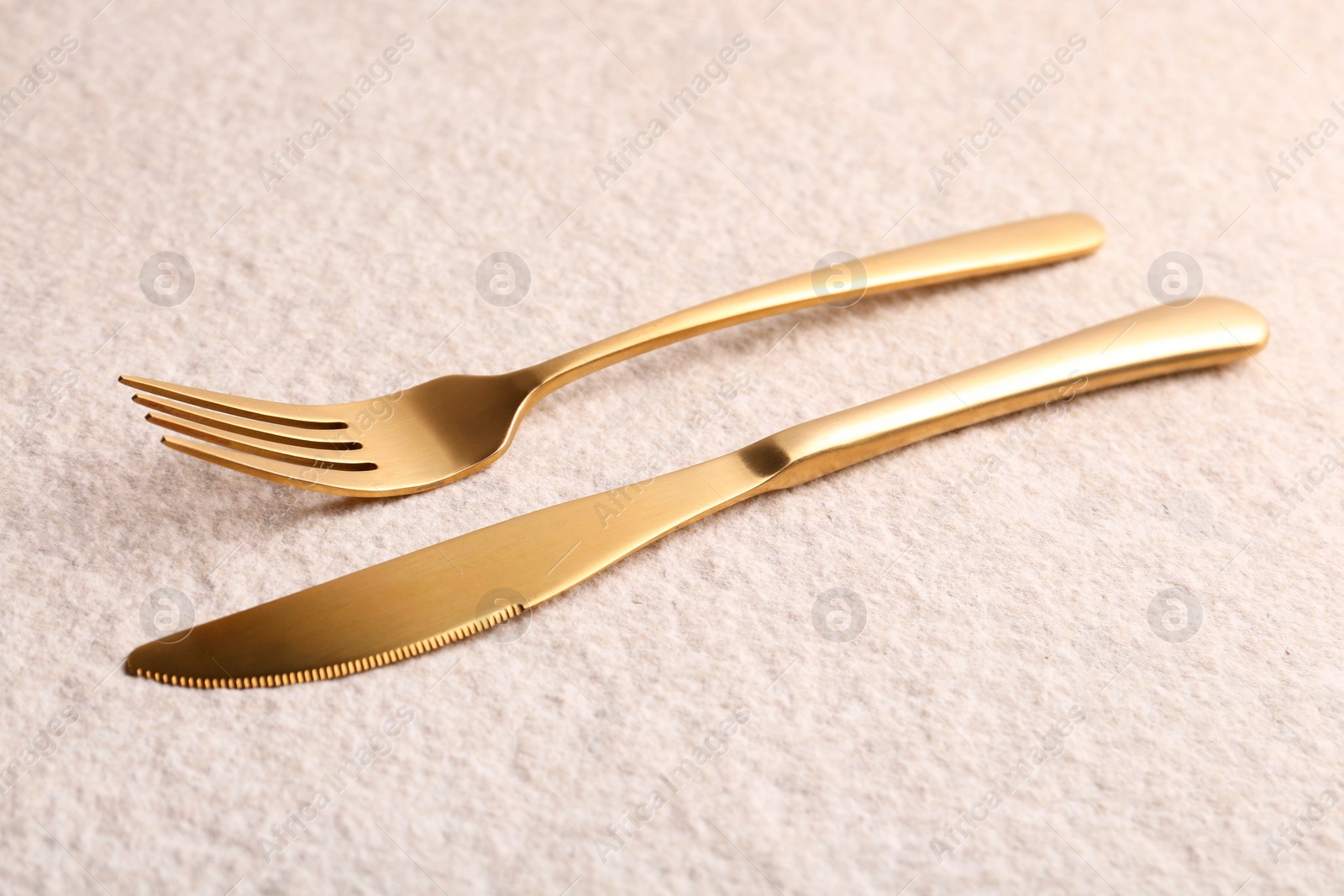 Photo of Stylish cutlery. Golden knife and fork on light textured table