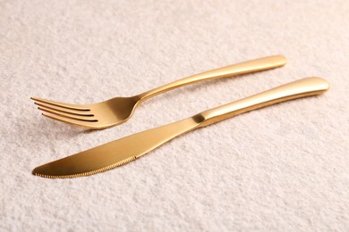 Stylish cutlery. Golden knife and fork on light textured table