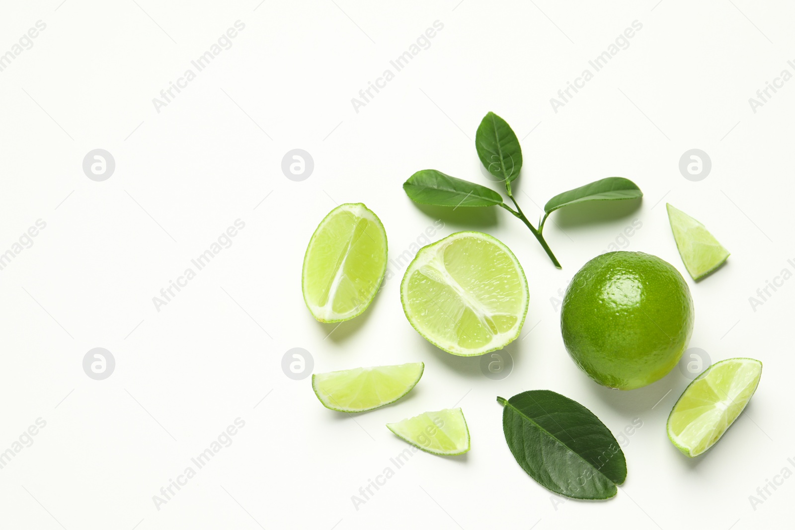 Photo of Whole and cut fresh ripe limes with green leaves on white background, flat lay