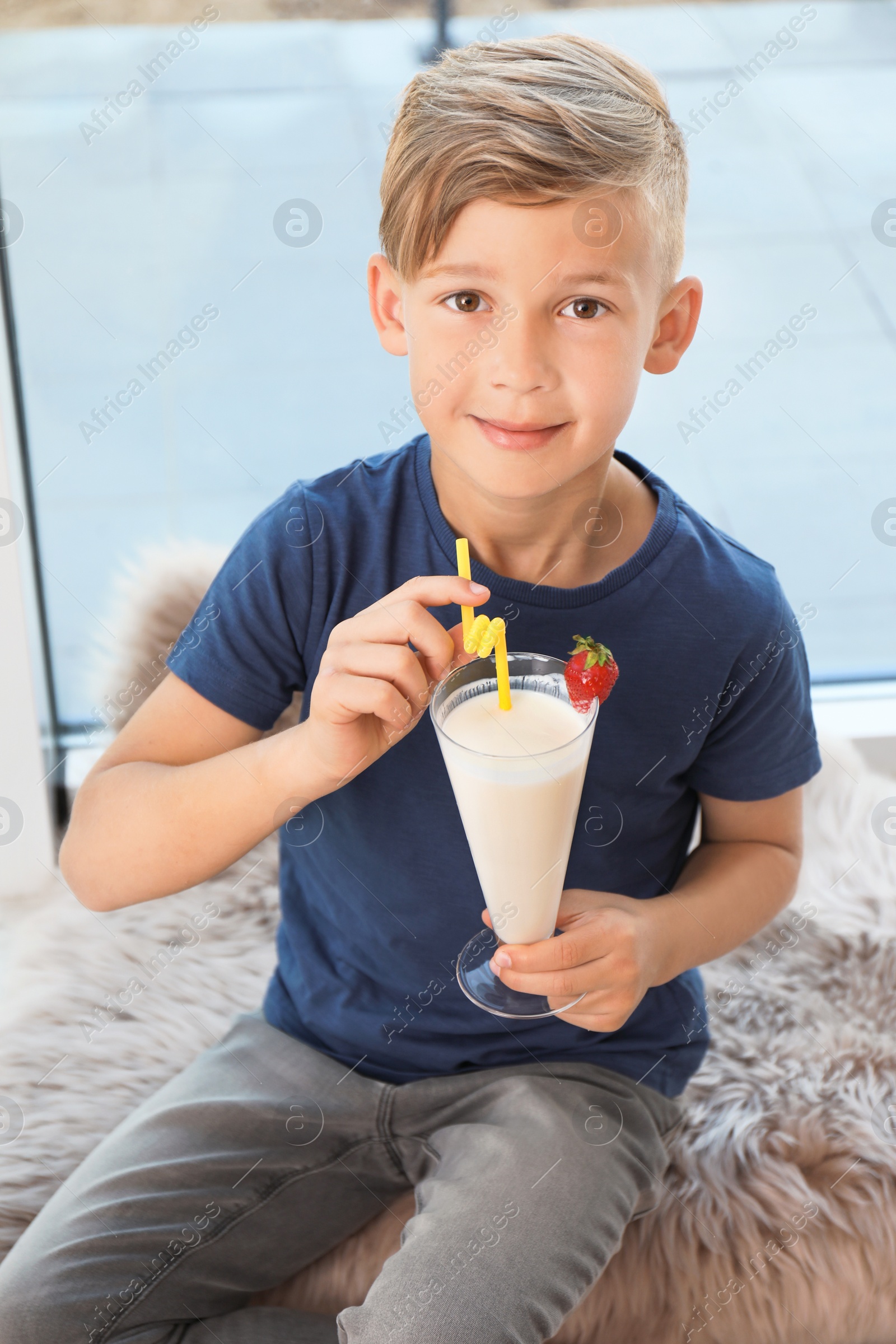 Photo of Little boy with glass of milk shake near window indoors