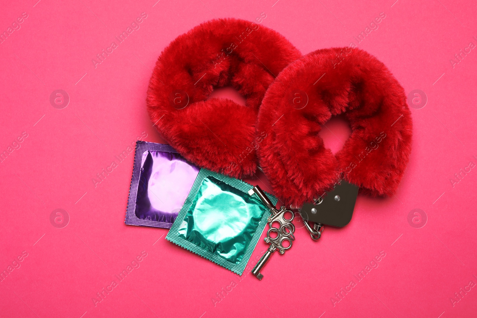 Photo of Furry handcuffs and condoms on pink background, top view. Sex game