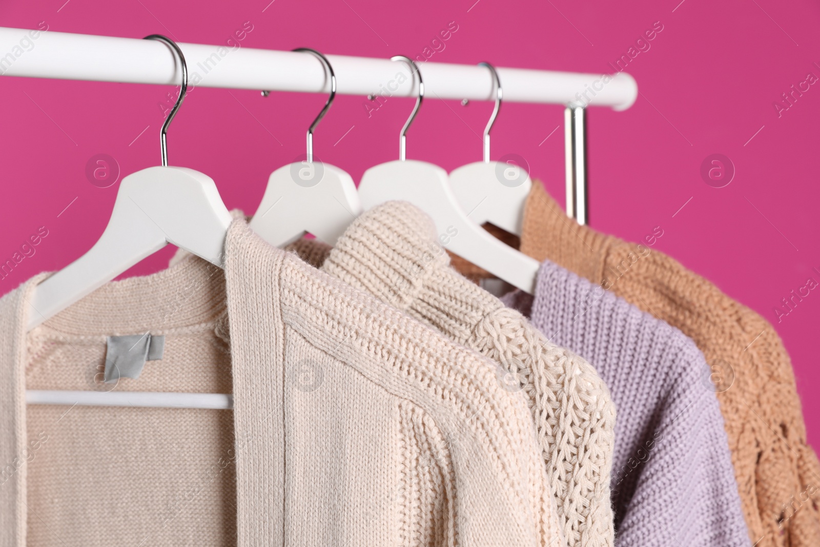 Photo of Collection of warm sweaters hanging on rack against color background, closeup