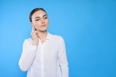 Photo of Young woman suffering from ear pain on light blue background. Space for text