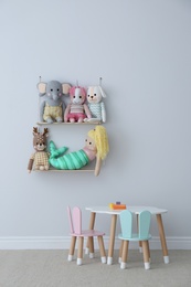 Photo of Table, chairs with bunny ears and collection of cute toys in child's room interior