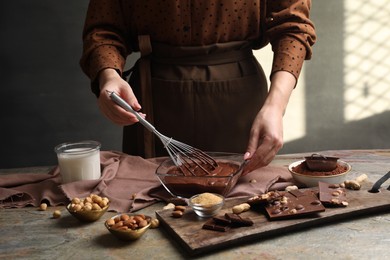 Photo of Woman mixing delicious chocolate cream with whisk at grey textured table, closeup