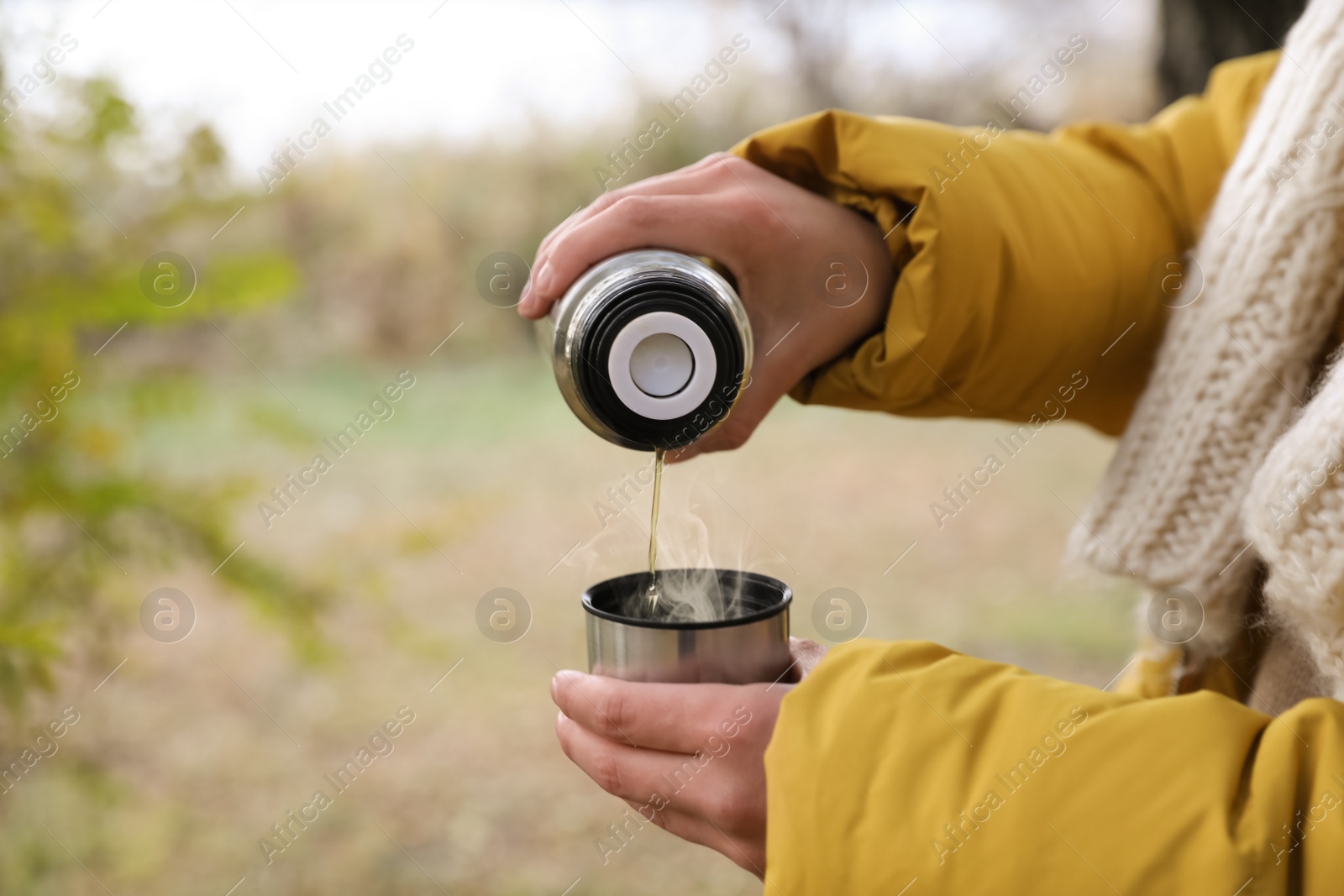 Photo of Woman pouring drink from thermos into cap outdoors, closeup. Space for text