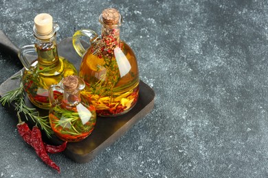 Photo of Cooking oil with different spices and herbs in jugs on light grey table, above view. Space for text