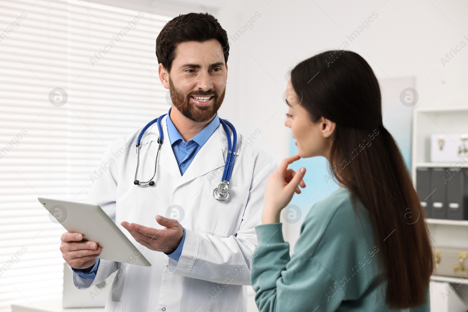 Photo of Doctor with tablet consulting patient during appointment in clinic